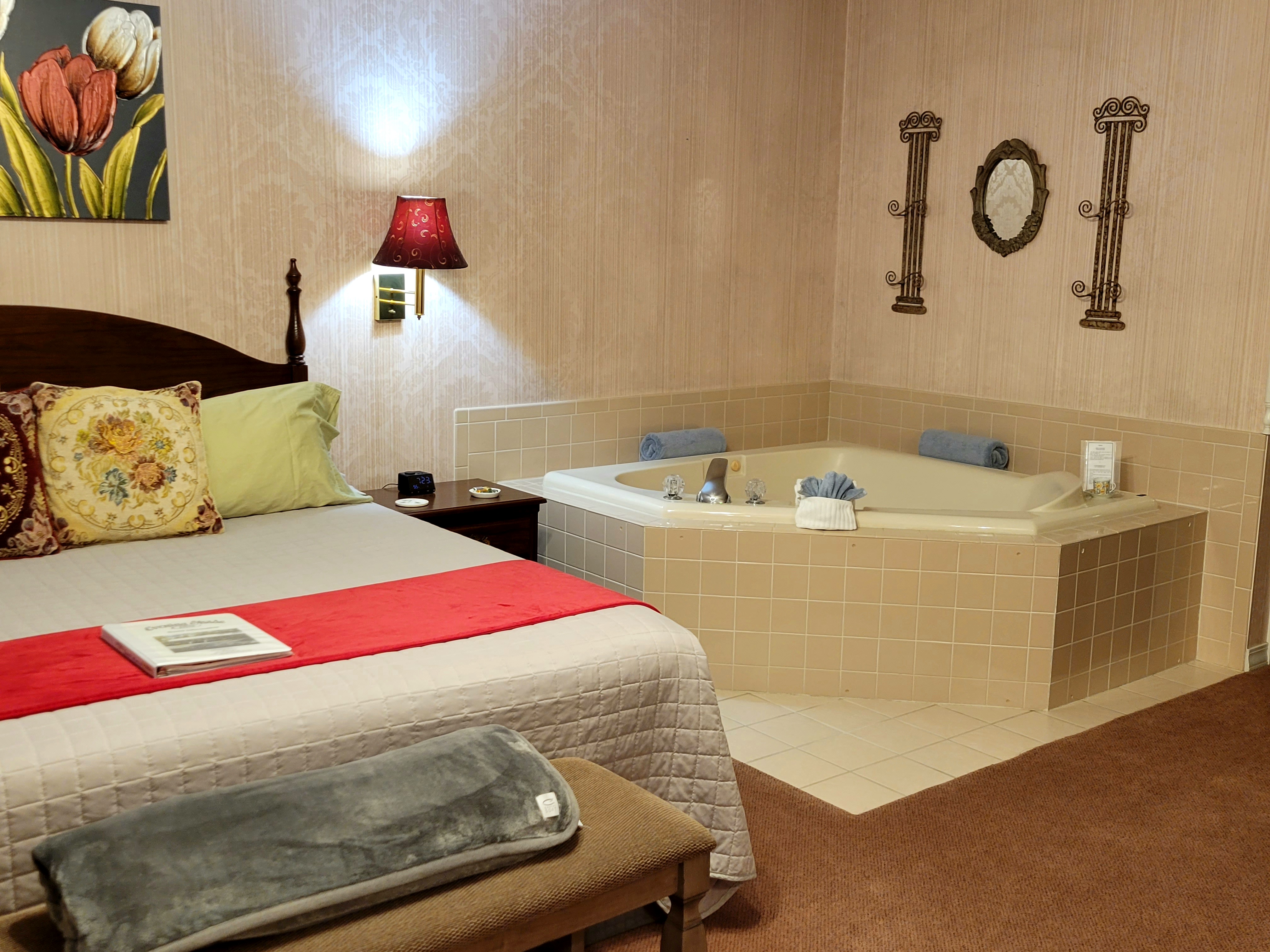 2-Person jetted tub in the corner of the guestroom. Pinkish tile surrounding. Towels are rolled and are decorating the sides of the tub. There is a painting on the left wall and a small mirror on the right side wall.
