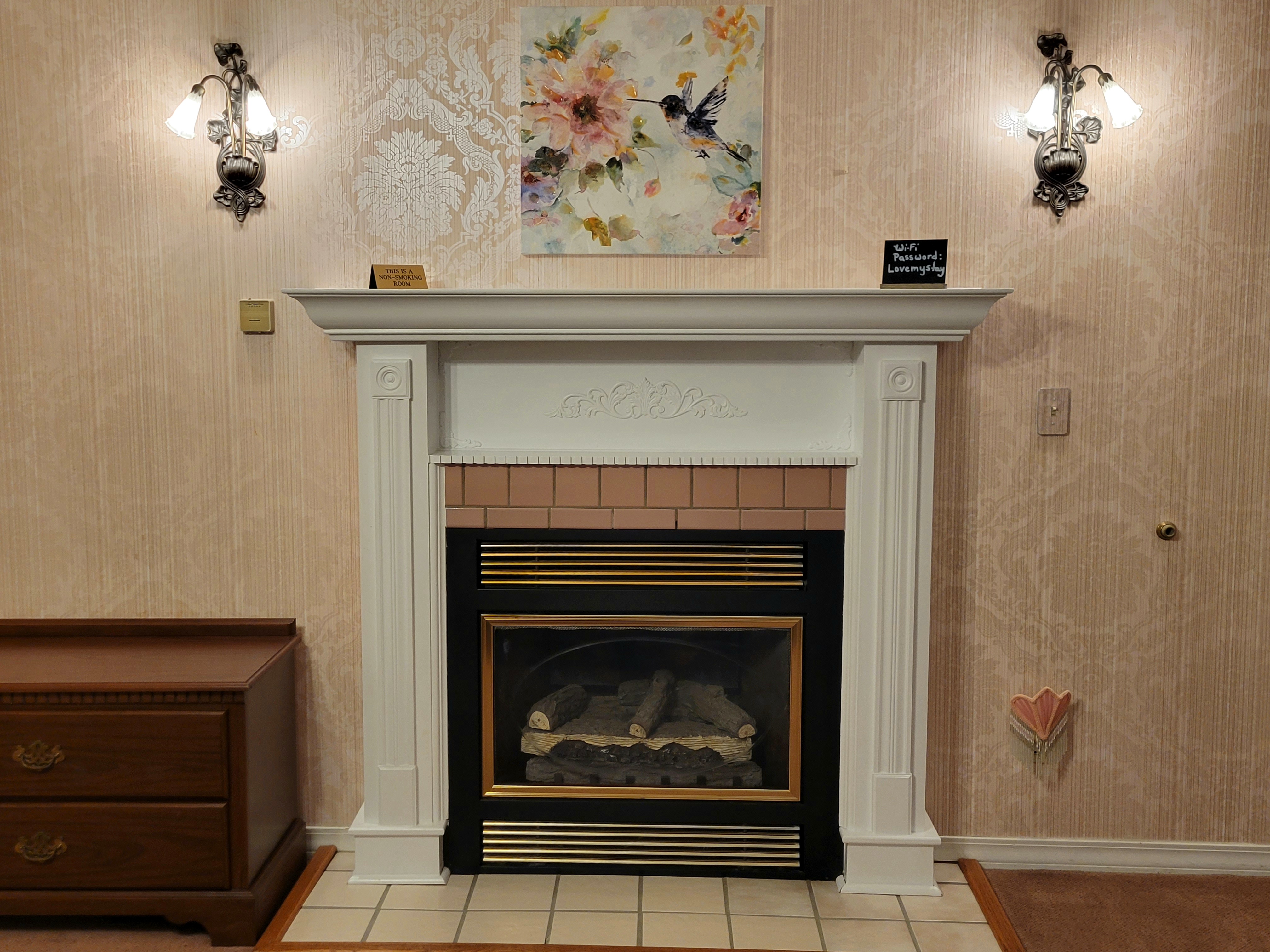 There is a gas fireplace and two wall sconses light with a floral painting hanging in the middle above the fireplace.