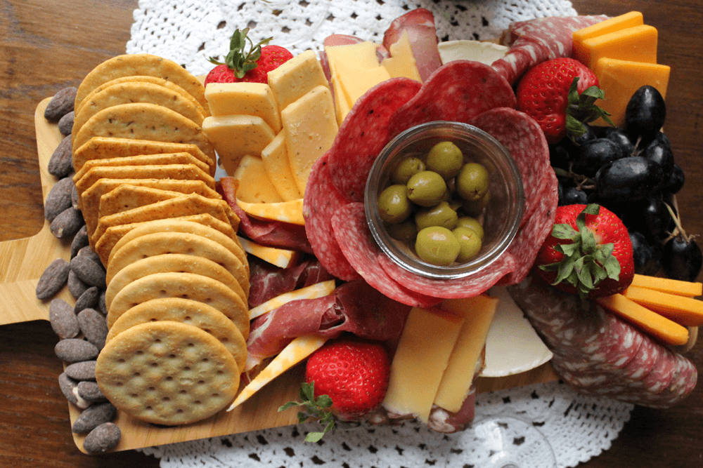 A beautifully arranged charcuterie board featuring assorted cheeses, cured meats, crackers, olives, strawberries, and grapes.