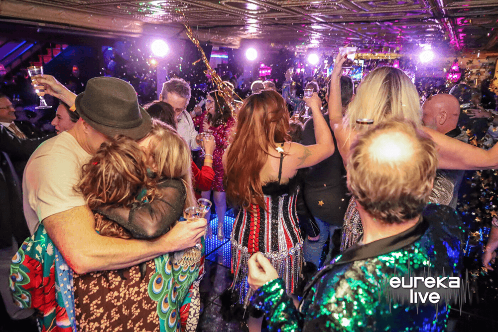 A lively crowd enjoys a festive party in a vibrant, decorated venue.