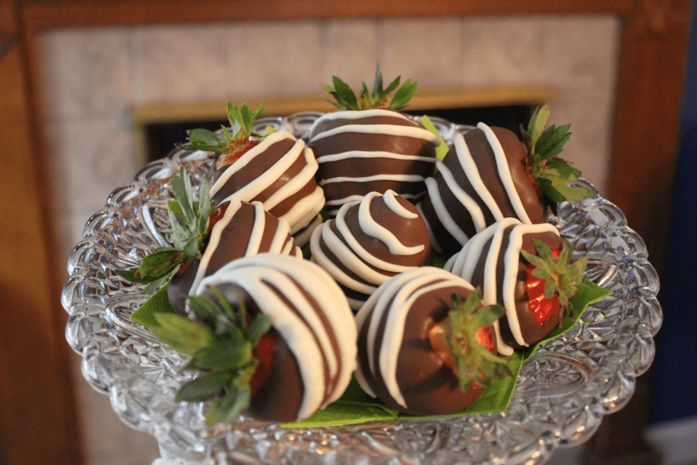 A crystal plate holds several chocolate-covered strawberries drizzled with white chocolate.