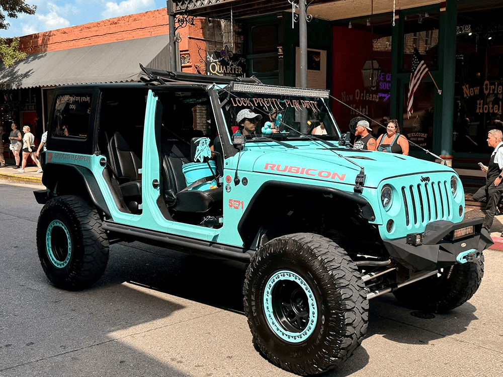 A light blue Jeep Rubicon with no doors parked on a busy street.