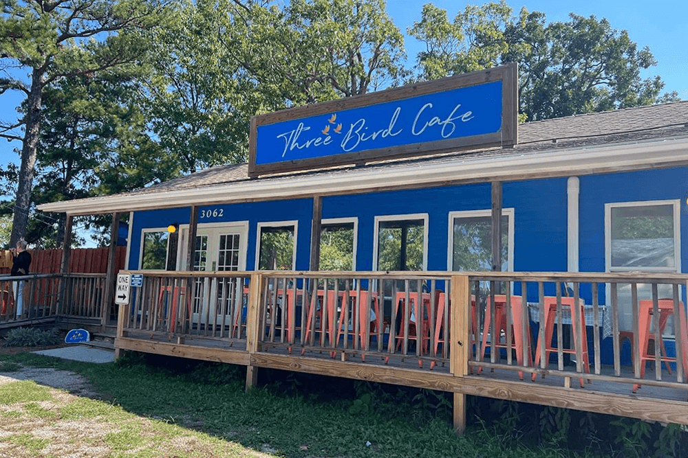 A bright blue cafe with a wooden deck and the sign "Three Bird Cafe" above the entrance.