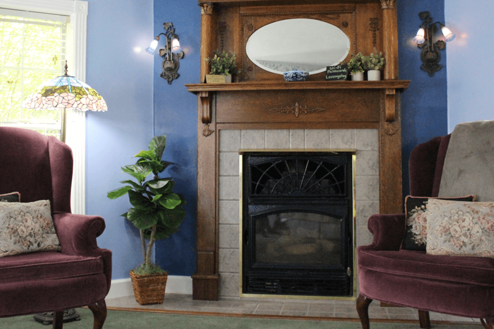 Cozy living room featuring two plush armchairs, a decorative fireplace, and a stained glass lamp.