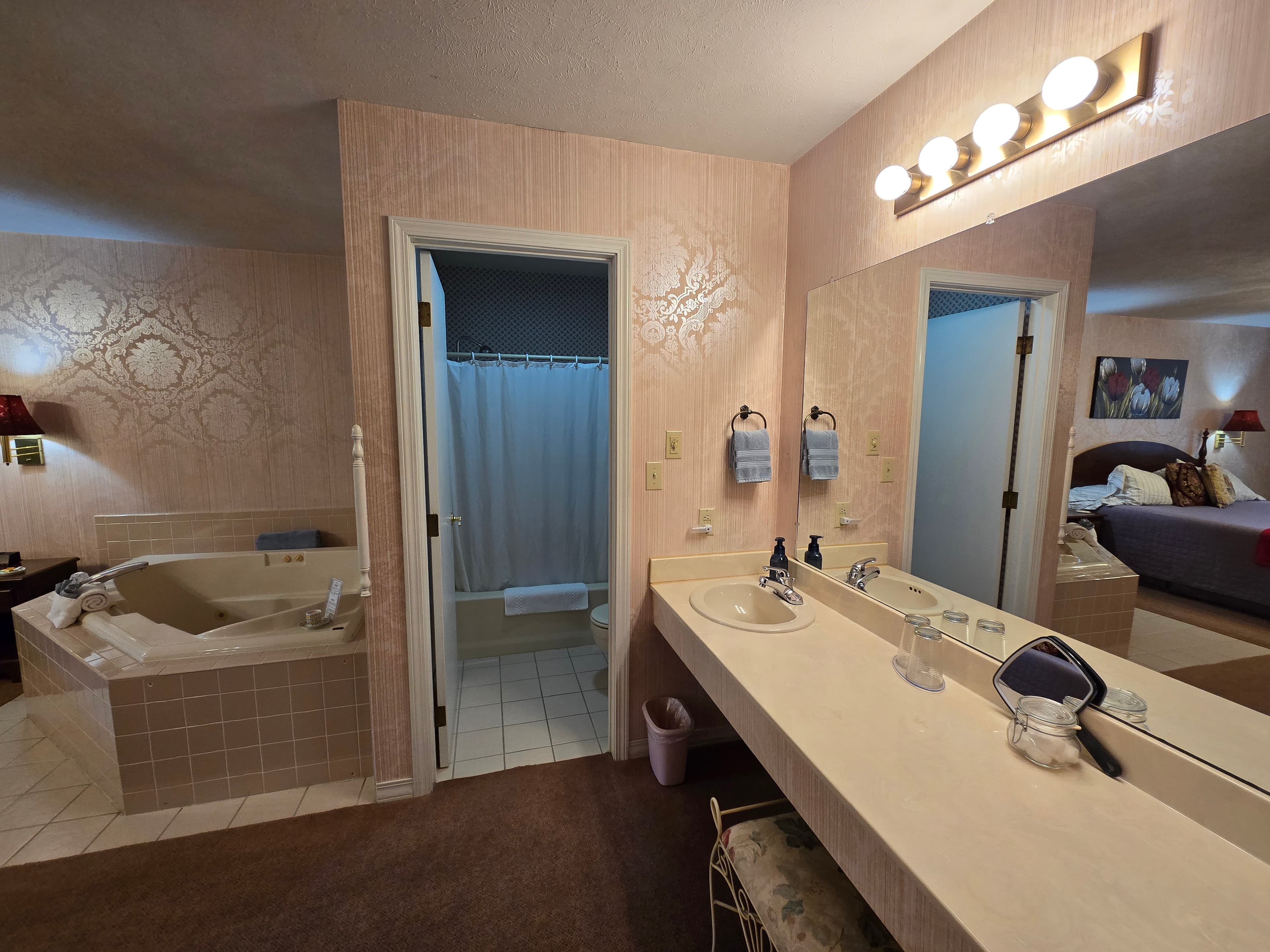 Bathroom with double vanity, tiled corner soaking tub, and open doorway to a shower/toilet area.