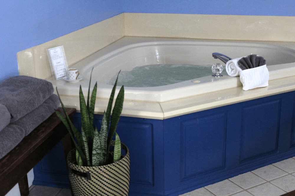 A corner jacuzzi tub next to a potted plant and a towel neatly arranged on a bench.